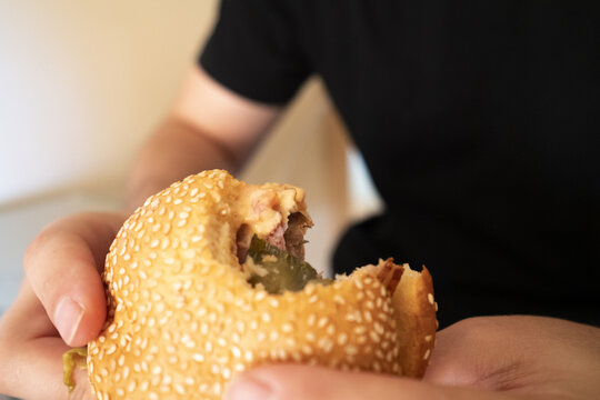 A person holding a sesame seed burger with a bite taken out, showcasing delicious toppings and textures for food lovers and culinary enthusiasts.