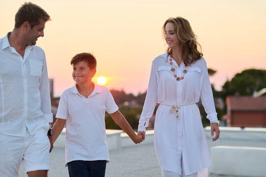 Family Walking Hand in Hand on Rooftop Terrace at Sunset With Sea View
