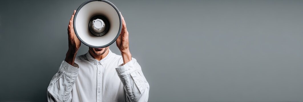A person with a megaphone is standing against a muted gray backdrop, arms and shirt visible