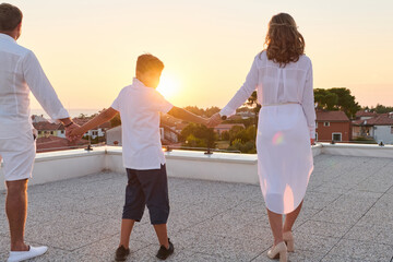 Obraz premium Family On Rooftop Balcony Holding Hands At Sunset With Sea View Over Coastal Town