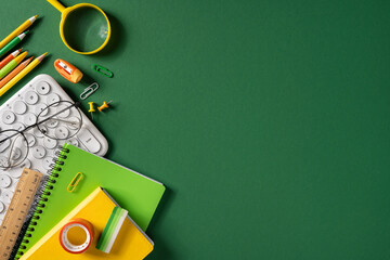 Obraz premium Back to school flat lay with green notebooks, pencils, keyboard and glasses on dark green background