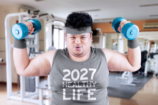 Overweight man exercising with dumbbells at the gym for a healthy 2027