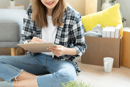 Move house, relocation. Woman using household checklist for new apartment Inside the room are cardboard boxes containing personal belongings and furniture. Move into a house or condominium