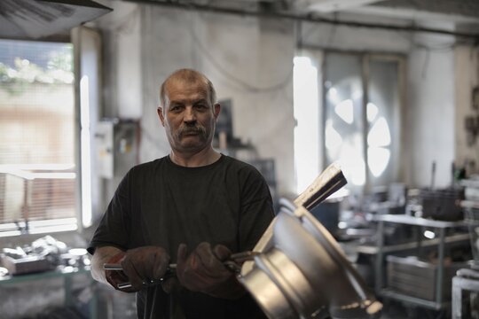 Mature worker with mustache looks at camera in workshop