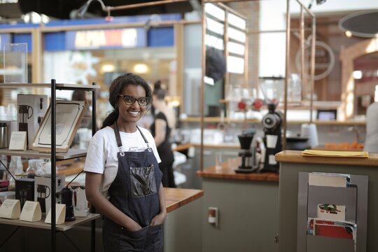 Friendly young barista smiling in her modern coffee shop