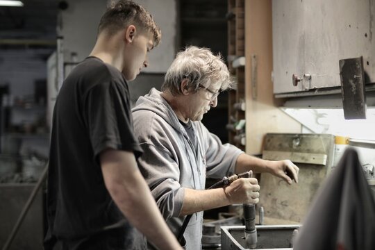 Senior craftsman teaches young apprentice in workshop