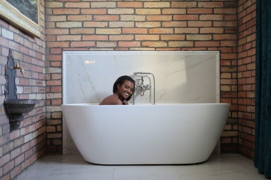 Happy young woman relaxing in a freestanding bathtub