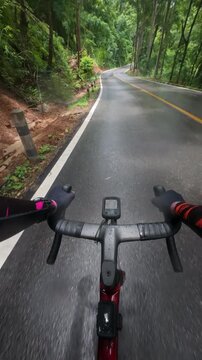 First-person point of view of a road cyclist riding along a wet mountain road after rainfall, surrounded by lush tropical forest. Water droplets on the handlebars and camera enhance the immersive expe
