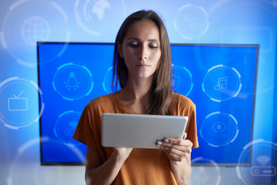 Woman using smart home application on digital tablet in front of television at home