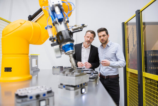 Two businessman observing industrial robots in factory