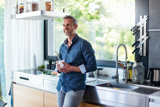 Smiling mature man at home in kitchen with cup of coffee