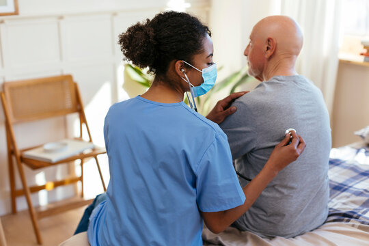 Nurse listening to senior patient's heartbeat using stethoscope at home
