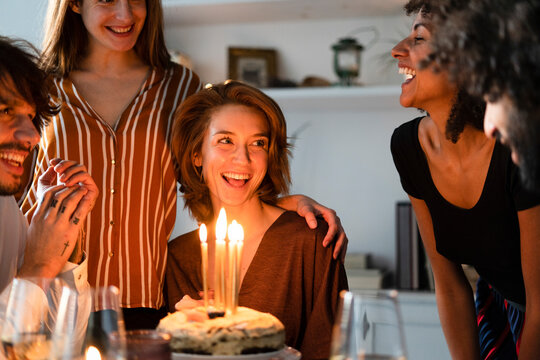 Friends surprising young woman with a birthday cake with burning candles