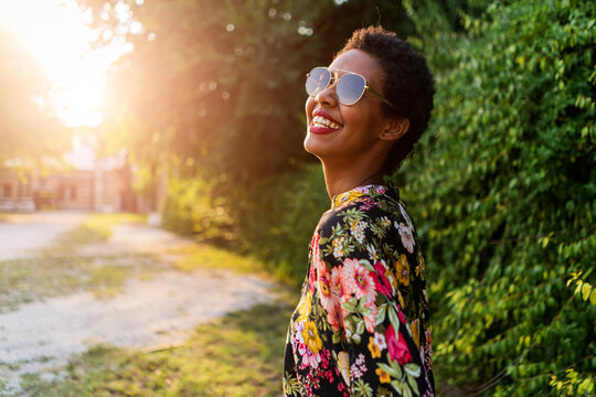 Happy young woman wearing sunglasses outdoors at sunset