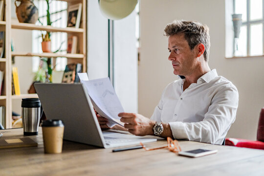 Focused businessman using laptop and reviewing documents at desk
