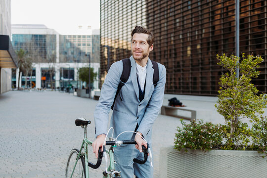 Male commuter wearing back pack walking with bicycle on road in city