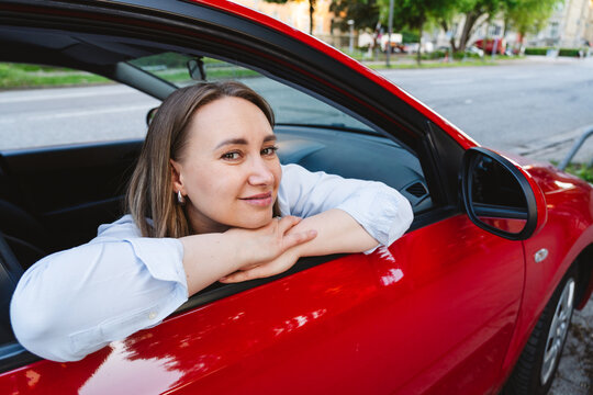 Woman leans on the window of a red car taking a quiet pause