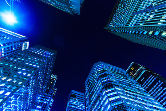 Futuristic cyber-blue city skyline of Tokyo's financial district from a dynamic looking-up perspective.