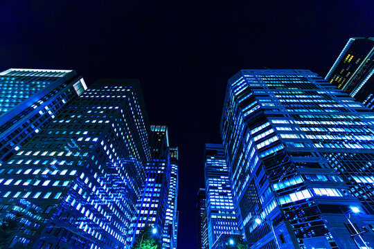 Dynamic low-angle looking up perspective of futuristic corporate skyscrapers lining a dark night sky canyon in Tokyo.