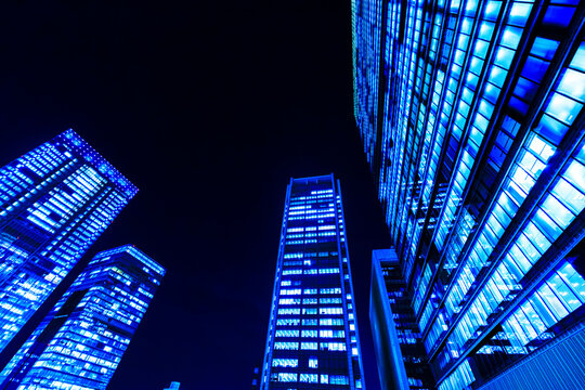 Dramatic low-angle view of four illuminated office skyscrapers in Tokyo at night with cyber-blue lights and central copyspace.