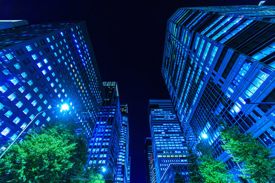Dynamic low-angle looking up perspective of futuristic corporate skyscrapers lining a dark night sky canyon in Tokyo.