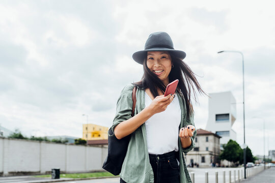 Happy young woman wearing hat standing with smart phone