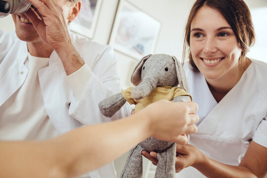 Nurse distracting child with toy while doctor using surgical microscope to check ears