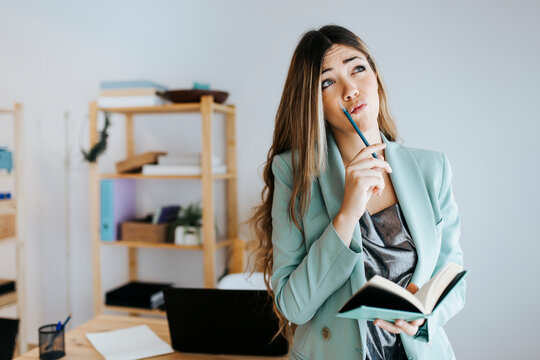 Businesswoman thinking while writing in diary at office