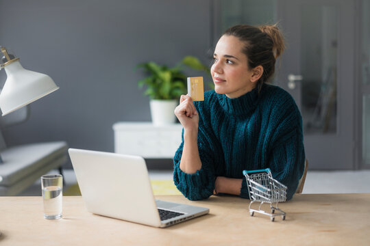 Portrait of content woman with laptop and credit card sitting at desk at home
