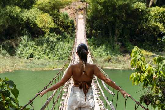 Woman stands on a wooden hanging bridge over a river in Bohol