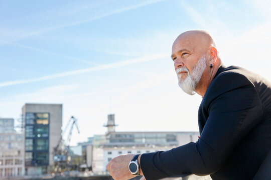 Elegant businessman standing in the city, leaning on railing, enjoying the view