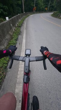 First-person point of view of a road cyclist riding through a winding mountain road surrounded by lush tropical forest. The immersive footage captures the experience of navigating a sharp curve during