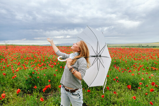 Mature woman holds umbrella in poppy field feeling optimistic