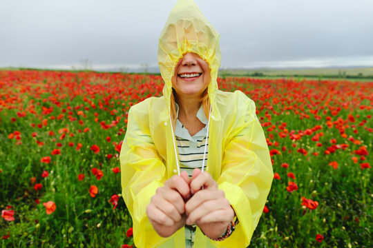 Smiling woman hides face in yellow raincoat at outdoor poppy field