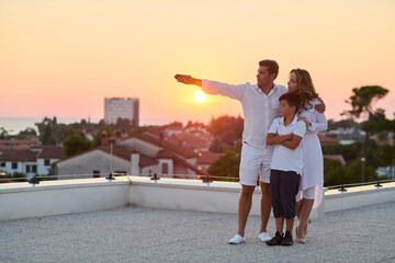 Obraz premium Family on Rooftop Balcony at Sunset Over Sea Enjoying Together on Summer Terrace