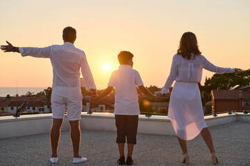 Obraz premium Family On Rooftop Balcony Holding Hands At Sunset With Sea View And Warm Summer Evening