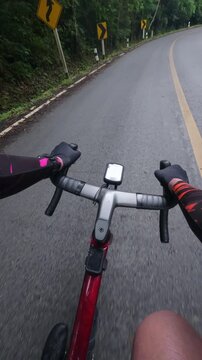 First-person point of view of a road cyclist riding through a winding mountain road while safely sharing the roadway with an oncoming vehicle. Surrounded by lush tropical forest, the footage highlight