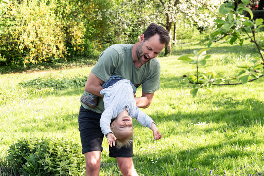 Father holds his smiling son upside down in the spring garden