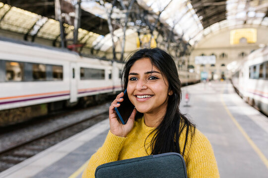 Smiling woman looking away while talking on mobile phone on railroad station platform