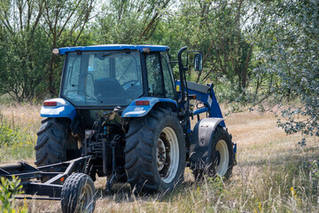 Obraz premium Blue tractor mowing grass in a rural field