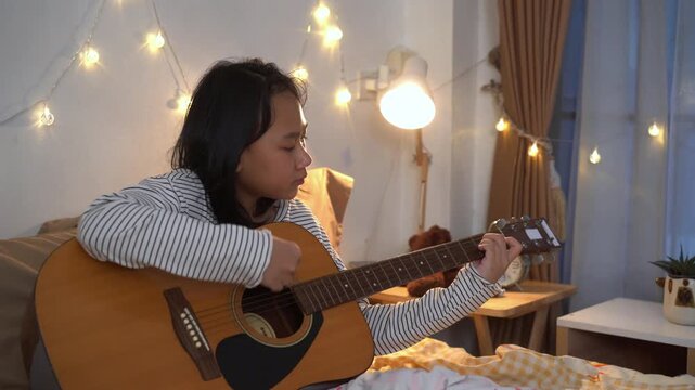 Young Girl carefully practicing chords on an acoustic guitar in Cozy Bedroom at Home	