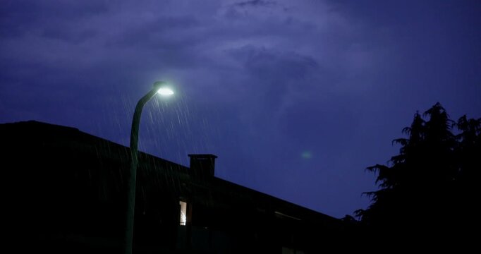 Rain Falls Under a Glowing Streetlight During a Night Thunderstorm in Bassano del Grappa, Italy - Handheld Shot
