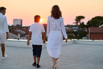 Obraz premium Family Walking on Rooftop Terrace at Sunset With Sea View on Summer Vacation