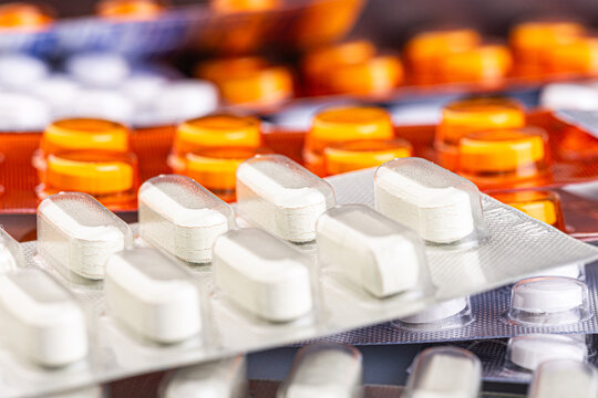 White caplets and orange tablets sit in blister packs on a clean surface. Healthcare concept for pharmacy, medication, treatment, and safe dosage.