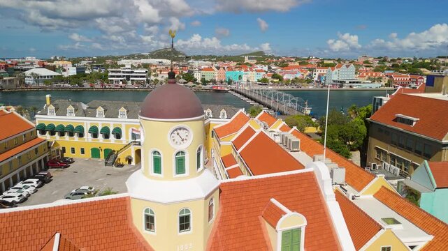 Aerial orbit over Fort Church clock tower in Punda Willemstad Curacao reveals colorful colonial rooftops Queen Emma Bridge and cruise ship in harbor