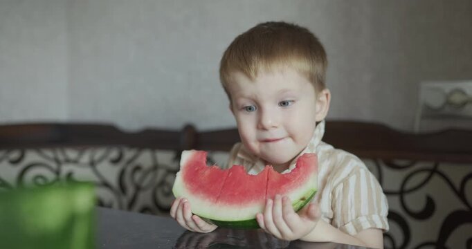 Cute little boy eating a big slice of juicy watermelon at home