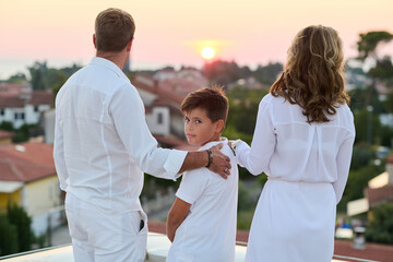 Obraz premium Family on Rooftop Balcony at Sunset With Sea View Parents and Son Embracing Outdoors