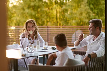 Family Enjoying Coffee on Sunny Balcony Terrace With Couple and Child Relaxing at Home © .shock