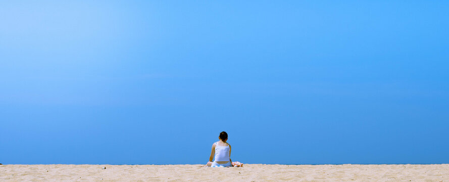 Blue sunny sky, warm orangey beach with a girl sunbathing