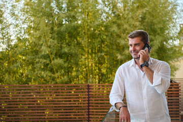 Obraz premium Man Talking on Phone While Relaxing on Home Balcony With Lush Green Background